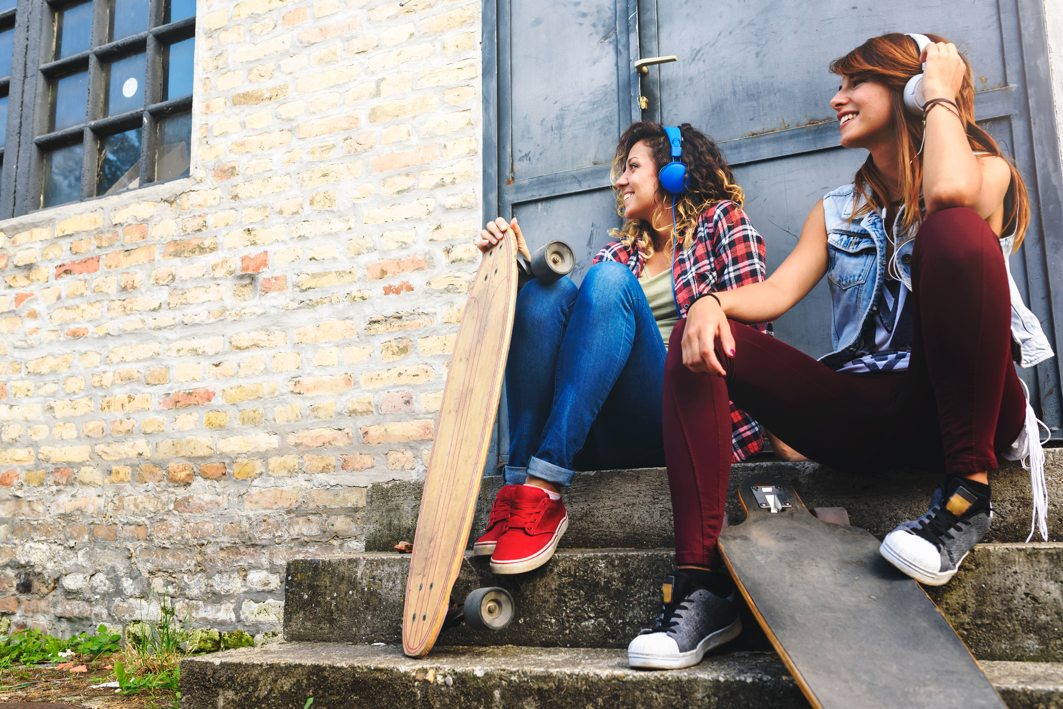 Gen Z girls sitting in the street hanging out listening music with earphones and smartphone