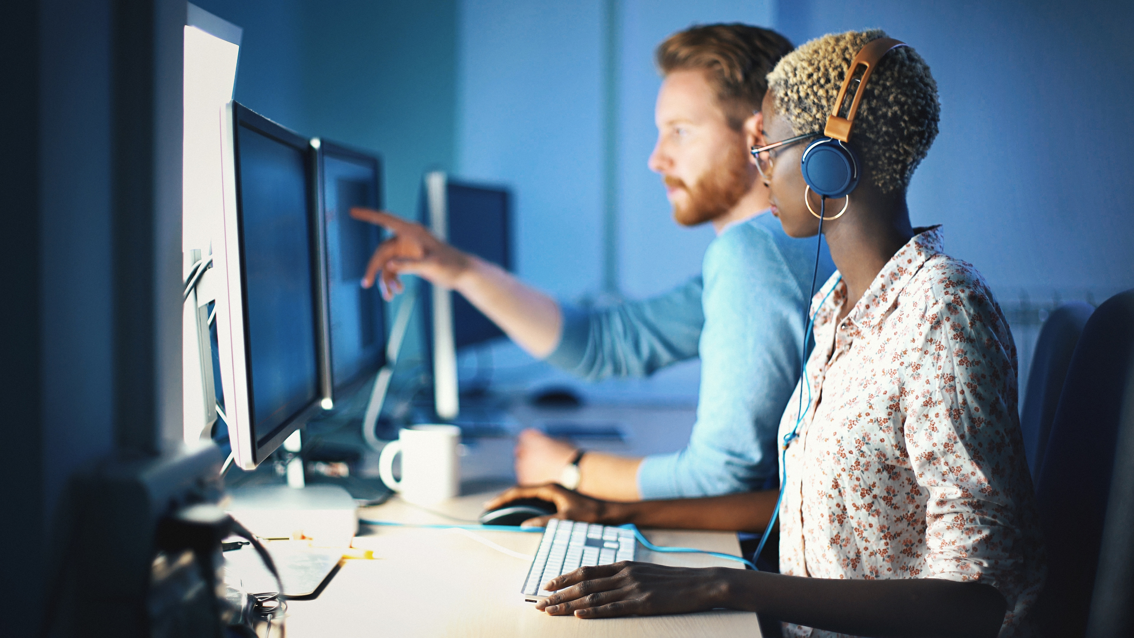 Closeup side view of African american woman and red hair caucasian guy working late at an IT office. They are checking the lines of the code and trying to find the error.