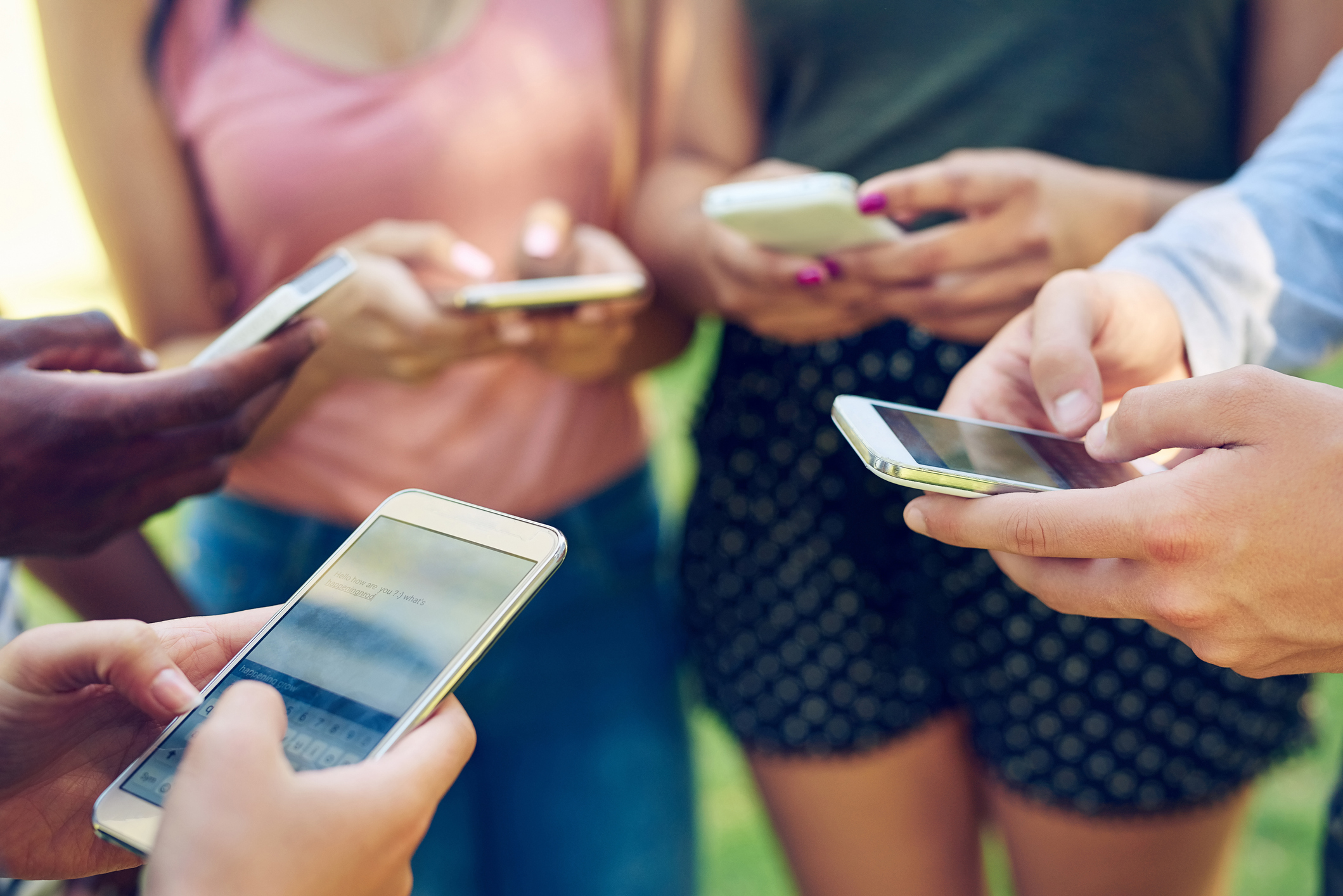 Cropped shot of a group of friends using their phones together outdoors