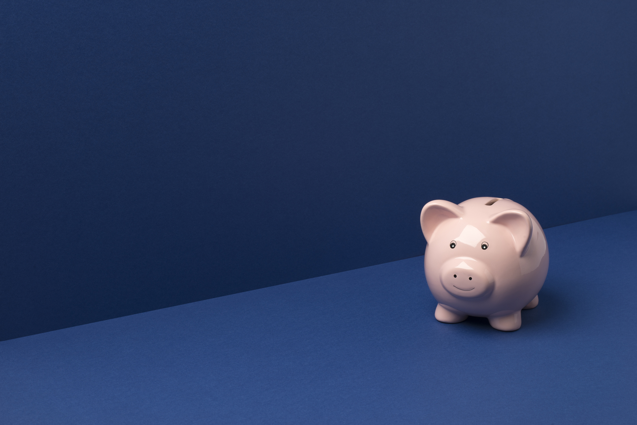 Small piggy bank on a blue wall and floor background with copy space