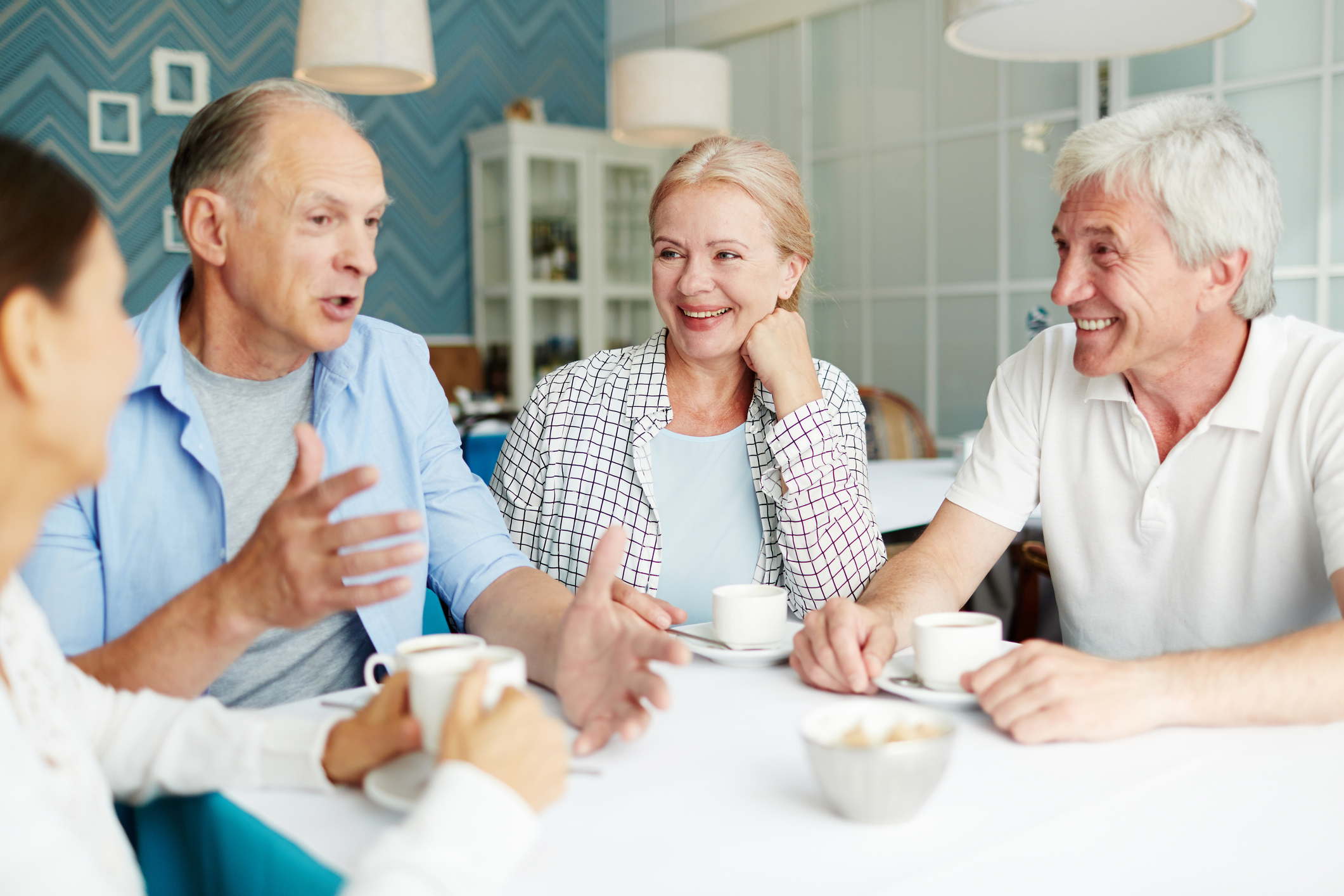 Happy and friendly senior men and women having talk by cup of tea in cafe