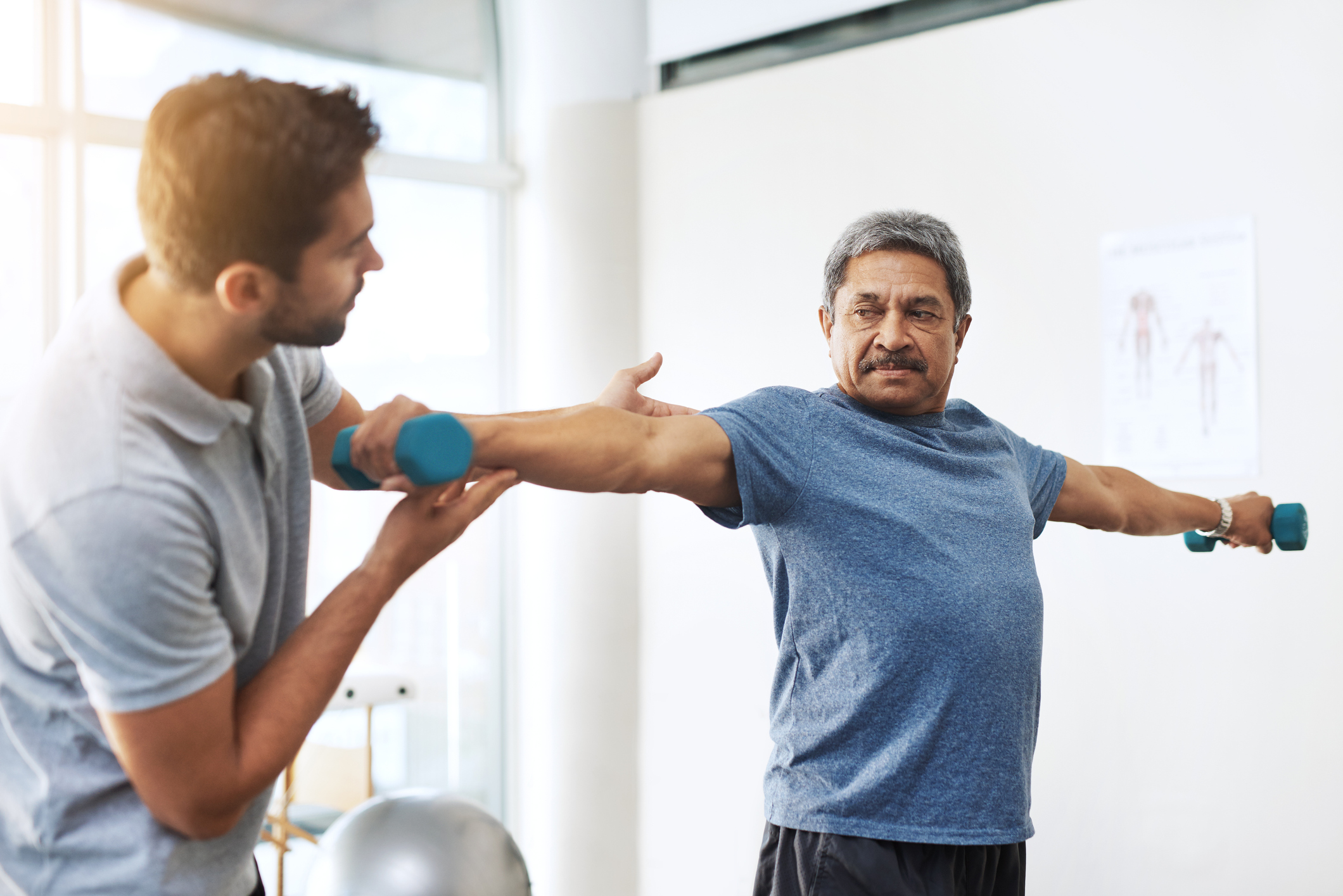 Shot of a young male physiotherapist helping a mature male patient with movement exercises at a clinic