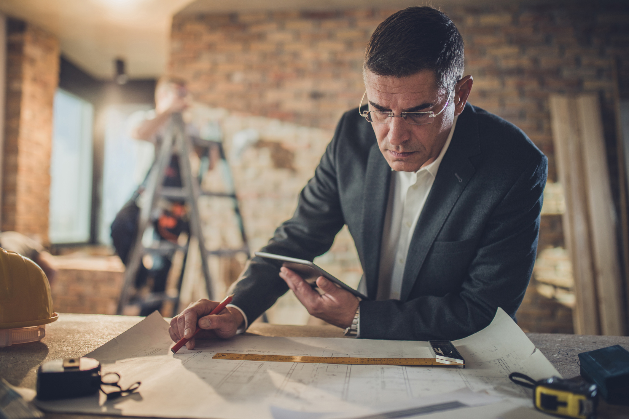 Mid adult male architect going through housing plan at construction site while using digital tablet. There are people in the background.