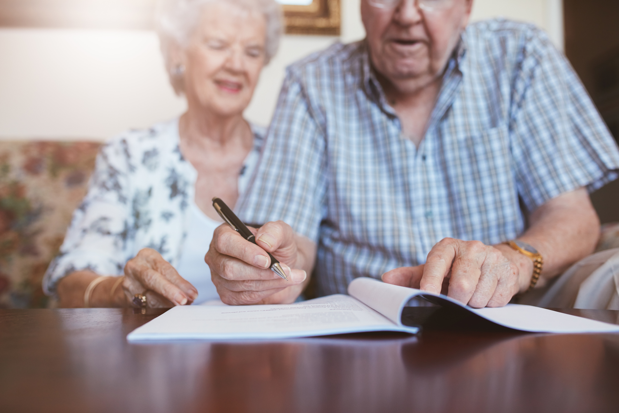 Senior couple signing retirement documents. Elderly caucasian man and woman sitting at home and signing some paperwork, focus on hands.