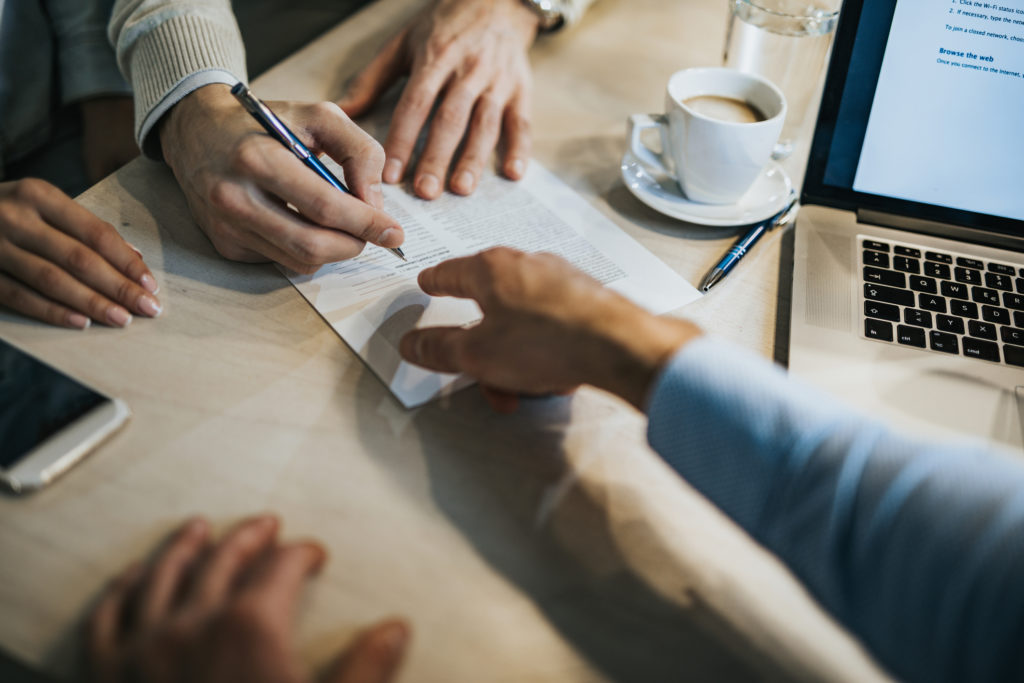 Unrecognizable man signing a contract while financial advisor is aiming at the place he need to sign.