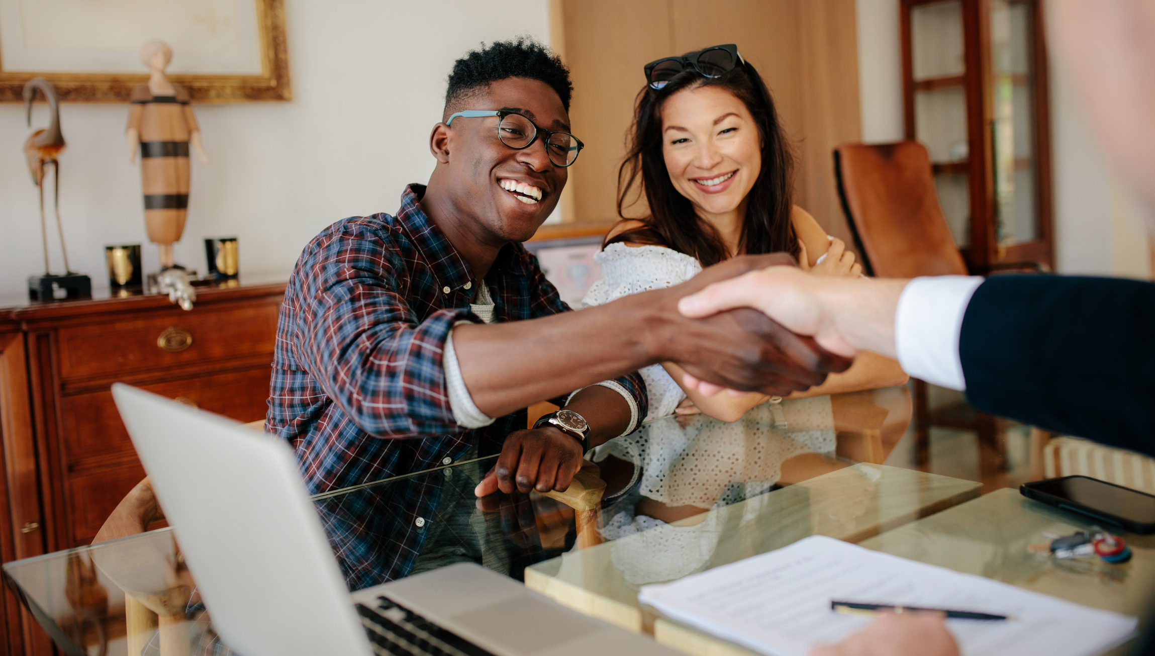 Happy property owners shaking hands with real estate broker after a deal. Young couple handshaking real estate agent after signing contract.