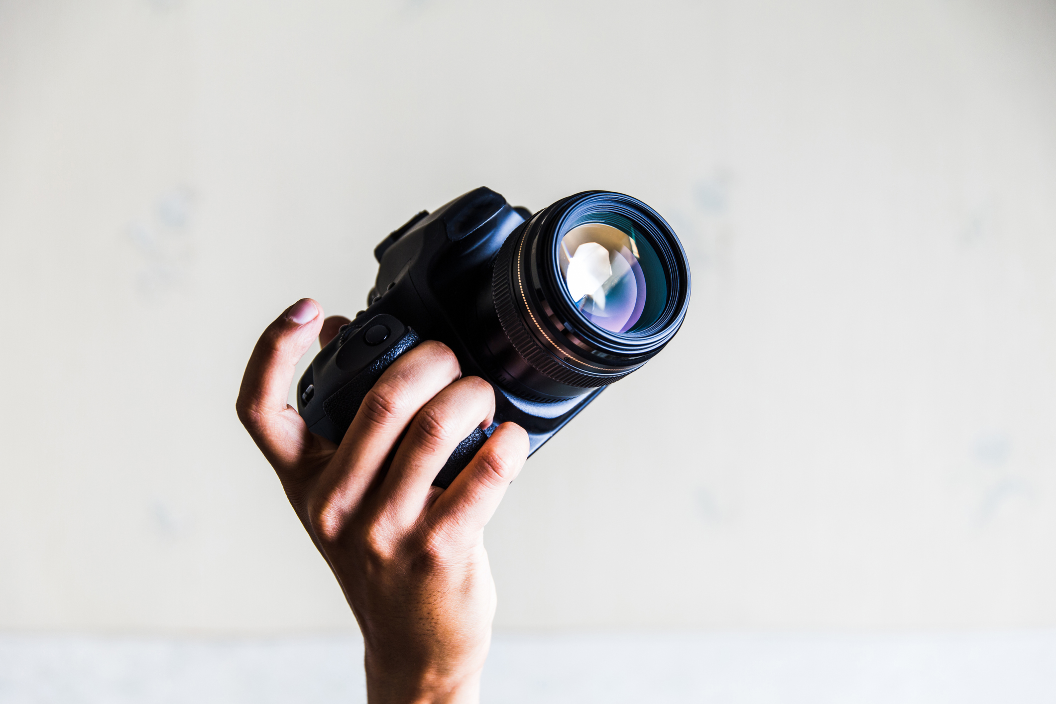 a hand holding a DSLR against white background