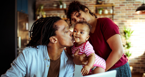 Photo of a family, with dad kissing the baby and searching on the computer.