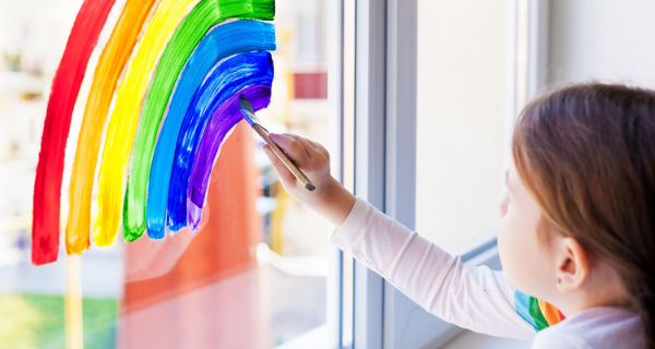 Girl painting a colorful rainbow on a window.