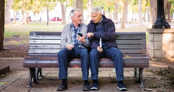 Image of two seniors sitting on a park bench pointing to something on a mobile devvce.