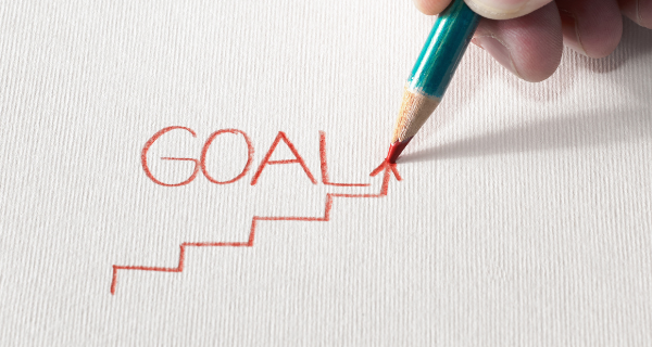 Image of someone writing the word “goal” in red pencil.