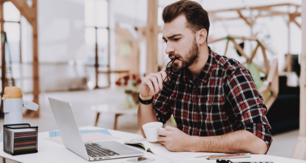 Image of someone sitting at a desk, drinking coffee, reading a blog on a a laptop.