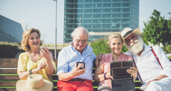 Image of seniors sitting on a bench using technology.